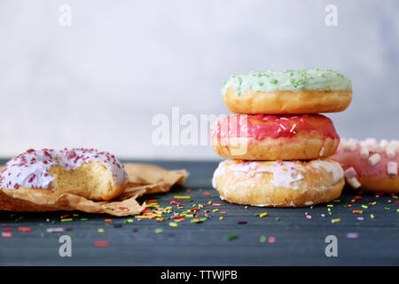 Leckere bunte Donuts auf der hölzernen Tisch gegen unscharfen Hintergrund, Ansicht schließen Stockfoto