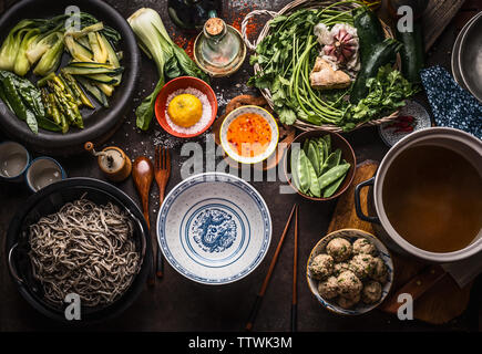 Asiatische Nudelsuppe Zutaten: verschiedenen frischen und gekochten grünen Gemüse, Kräuter und Gewürze, Frikadellen, Soba Nudeln und Stäbchen um leere Asien Stockfoto