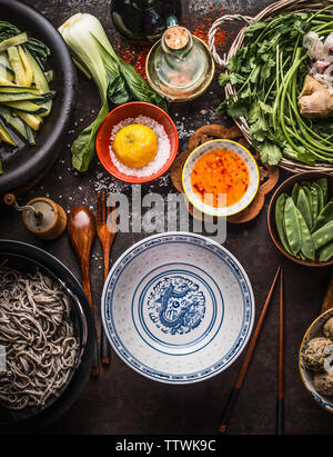 Leere asiatische Schale mit Essstäbchen und Zutaten für Nudeln essen mit grünem Gemüse und Soba auf dunklem Hintergrund im Landhausstil mit Küchengeräten, oben Stockfoto