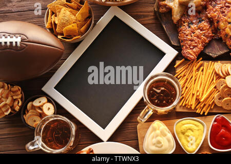 Rugby Ball, Rahmen und leckere Snacks mit Bier auf hölzernen Tisch Stockfoto