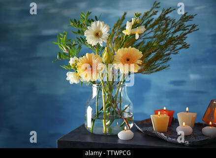 Schöne Blumen in Vase mit Kerzen auf blauem Hintergrund Stockfoto