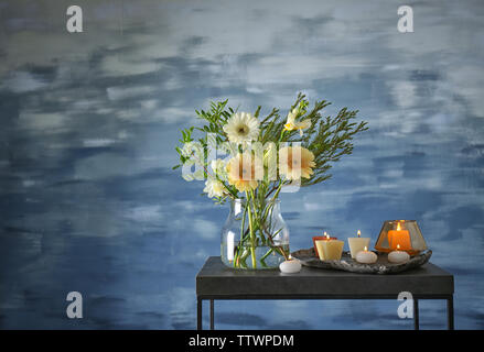 Schöne Blumen in Vase mit Kerzen auf blauem Hintergrund Stockfoto