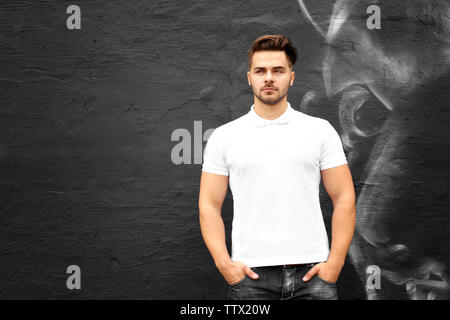 Junger Mann in Leer Poloshirt gegen Graffiti, Wand Stockfoto