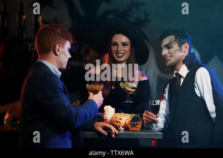 Junge Leute in Kostümen trinken Cocktails an Halloween Party Stockfoto