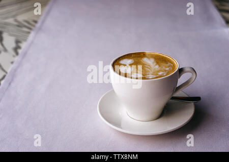 Weißer Becher auf einer Untertasse mit Cappuccino und schönen herzförmigen Milchschaum Stockfoto
