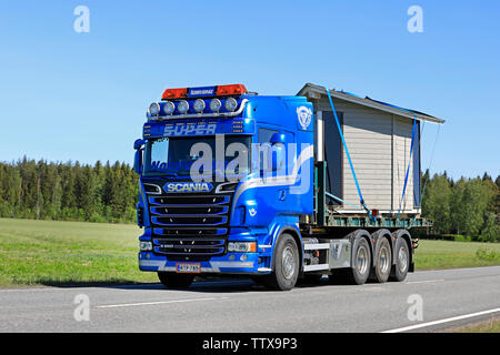 Somero, Finnland. 31. Mai 2019. Schön angepasste blaue Scania R560 Lkw Norrvidinge schleppt eine Holzhütte entlang der Straße an einem sonnigen Tag im Sommer. Stockfoto