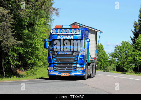 Somero, Finnland. 31. Mai 2019. Schön angepasste blaue Scania R560 Lkw Norrvidinge schleppt eine Holzhütte entlang der Straße an einem sonnigen Tag im Sommer. Stockfoto