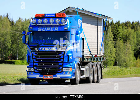 Somero, Finnland. 31. Mai 2019. Schön angepasste blaue Scania R560 Lkw Norrvidinge schleppt eine Holzhütte entlang der Straße an einem sonnigen Tag im Sommer. Stockfoto