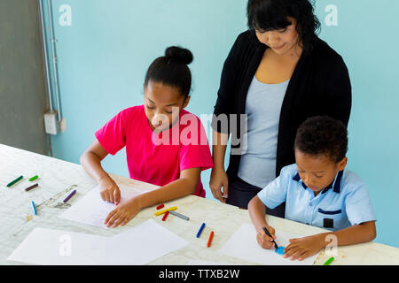 Junge Lehrerin afrikanischen amerikanischen Kids, die eine Art Lehre und Lehre wie Innen drinnen Zimmer in natürlichen Umgebungslicht zu zeichnen Stockfoto