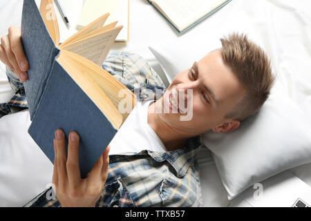 Hübscher junger Mann lesen Buch beim liegen auf dem Bett, Ansicht schließen Stockfoto