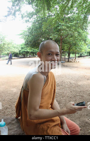 Mönch, der auf einem Felsbrocken sitzt und Textnachrichten aussahen, Tiger Temple, Sai Yok, Kanchanaburi, Thailand Stockfoto