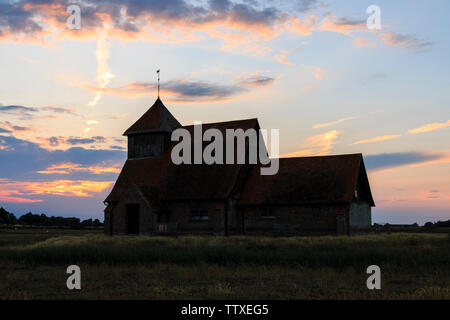 Die Kirche auf dem Sumpf. Der hl. Thomas Becket Kirche in Fairfield, Romney Marsh mit Sonnenuntergang, Sonnenuntergang. Einsame Gebäude auf Sumpfland, Sonnenuntergang mit Wolken. Stockfoto