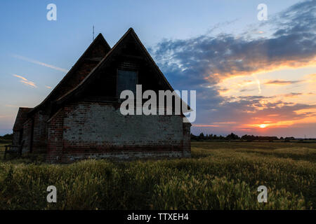 Die Kirche auf dem Sumpf. Der hl. Thomas Becket Kirche in Fairfield, Romney Marsh mit Sonnenuntergang, Sonnenuntergang. Einsame Gebäude auf Sumpfland, Sonnenuntergang mit Wolken. Stockfoto