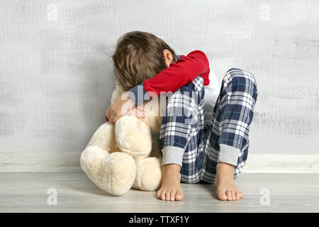 Traurige kleine Junge mit Teddybär sitzen auf dem Boden im leeren Zimmer Stockfoto