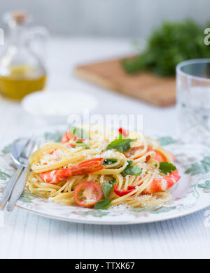 Schöne Platte mit einer Portion frische Garnelen Pasta, mit grünen Kräutern und Öl im Hintergrund Stockfoto