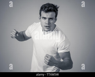 Junger attraktiver Mann in Rage suchen wütend in der Verteidigung Haltung und drohen Stanzen mit Faust in der wütenden umgekippt und wütenden Gesichtsausdruck isoliert Grau ba Stockfoto