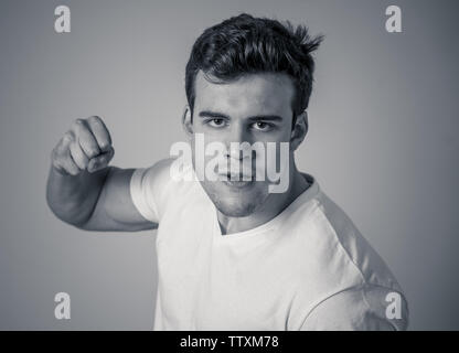 Junger attraktiver Mann in Rage suchen wütend in der Verteidigung Haltung und drohen Stanzen mit Faust in der wütenden umgekippt und wütenden Gesichtsausdruck isoliert Grau ba Stockfoto
