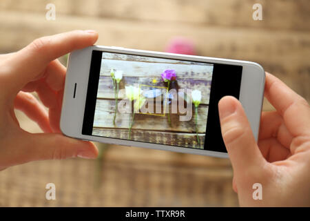 Weibliche Hände unter Foto von schönen Blumen mit Smartphone, Nahaufnahme Stockfoto