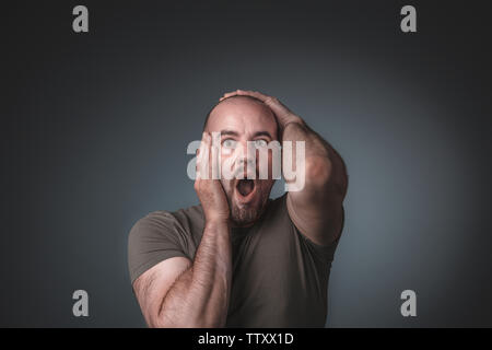 Studio Porträt eines Mannes hielt seinen Kopf, Ausdruck von Überraschung und Angst. Konzept der Schock. Stockfoto