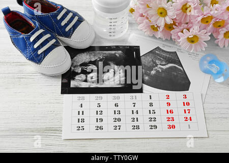 Baby warten Konzept. Ultraschall Foto und Kalender auf weißem Holz- Hintergrund Stockfoto