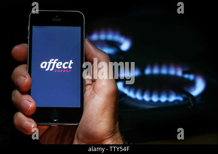 Ein Mann auf der Website Logo auf der Suche nach Energie unternehmen Energie Einfluss auf sein Handy vor seinem Gaskocher (Editorial nur verwenden) Stockfoto