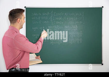 Junge männliche Lehrer neben Tafel auf der weissen Tafel Stockfoto