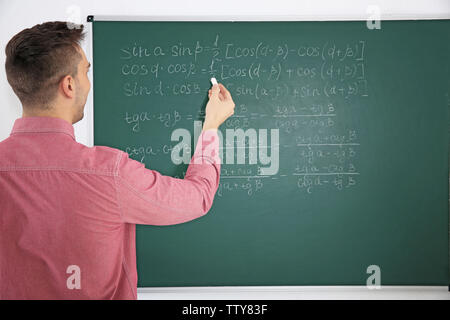 Junge männliche Lehrer neben Tafel auf der weissen Tafel Stockfoto