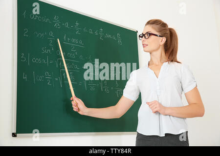 Junge Lehrerin mit Zeiger neben Blackboard auf weißem Hintergrund Stockfoto