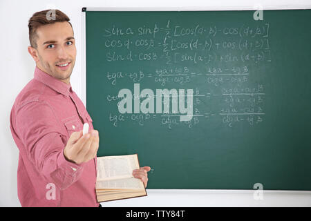Junge männliche Lehrer neben Tafel auf der weissen Tafel Stockfoto