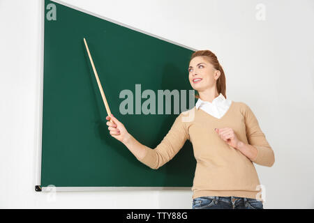 Junge Lehrerin mit Zeiger neben Blackboard auf weißem Hintergrund Stockfoto