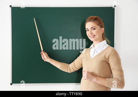 Junge Lehrerin mit Zeiger neben Blackboard auf weißem Hintergrund Stockfoto