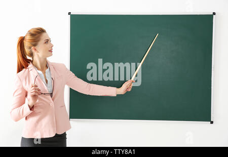 Junge Lehrerin mit Zeiger neben Blackboard auf weißem Hintergrund Stockfoto