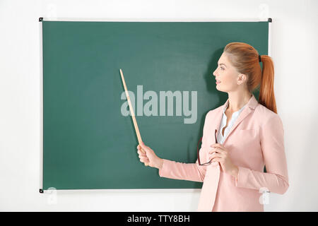 Junge Lehrerin mit Zeiger neben Blackboard auf weißem Hintergrund Stockfoto
