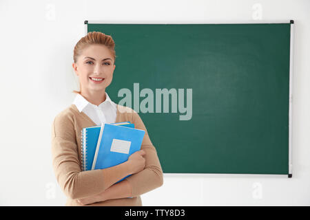 Junge Lehrer mit Copybooks neben Blackboard auf weißem Hintergrund Stockfoto