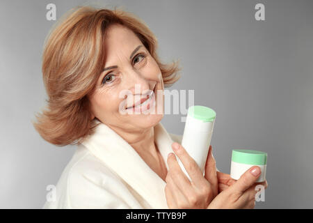 Wunderschöne ältere Frau mit Anti-aging Kosmetik auf grauem Hintergrund Stockfoto
