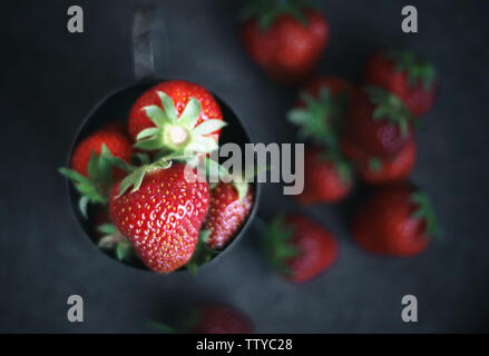 Reife Erdbeeren um ein Bügeleisen Becher verstreut. Dark Photo Stockfoto