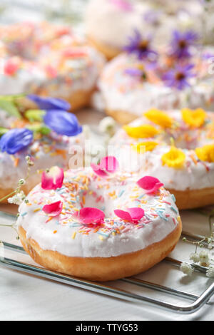 Delicious Doughnuts und Blumen auf backaufsatz und weißem Hintergrund, Nahaufnahme Stockfoto