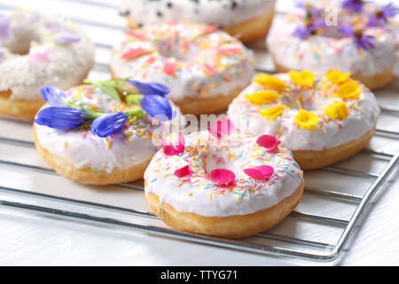 Delicious Doughnuts und Blumen auf backaufsatz und weißem Hintergrund, Nahaufnahme Stockfoto