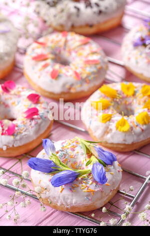 Delicious Doughnuts und Blumen auf backaufsatz und Holztisch, Nahaufnahme Stockfoto