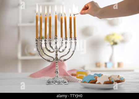 Weibliche hand Anwendung passen zu den Kerzen in der Menorah auf hölzernen Tisch. Chanukka Konzept Stockfoto