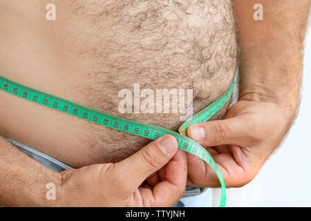 Ein Mann Maßnahmen seinen dicken Bauch mit einem Maßband. auf einem weißen Hintergrund. Stockfoto