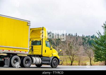 Leuchtend gelb Big Rig Tag cab Semi Truck für die lokalen Lieferungen mit aerodynamische Spoiler auf dem Dach Transportieren gelb Trocken van Auflieger auf dem Roa Stockfoto