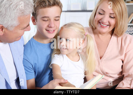 Niedliche Kinder mit großeltern Buch in Wohnzimmer Stockfoto