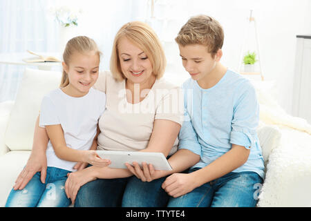 Süße Kinder und ihre Großmutter saß auf Sofa mit Tablet-PC Stockfoto