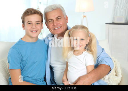 Niedliche Kinder mit Großvater sitzt auf einem Sofa im Wohnzimmer. Stockfoto