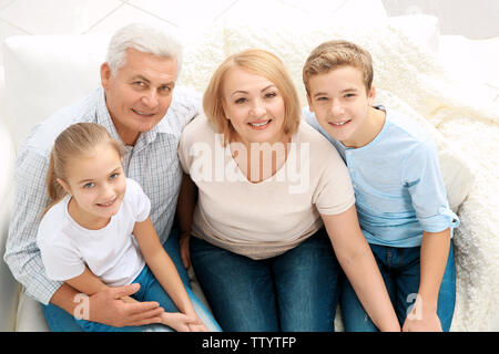 Niedliche Kinder mit Großeltern sitzen auf einem Sofa im Wohnzimmer. Stockfoto