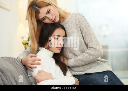 Schöne Frau umarmen depressiven Freund beim Sitzen auf dem Sofa zu Hause Stockfoto