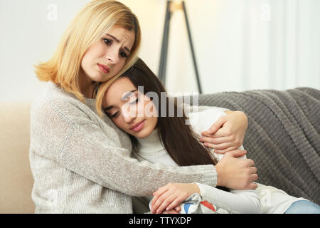 Schöne Frau umarmen depressiven Freund beim Sitzen auf dem Sofa zu Hause Stockfoto