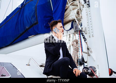 Seitenansicht der Unternehmer sitzen auf luxusyacht und Gespräch am Handy Stockfoto
