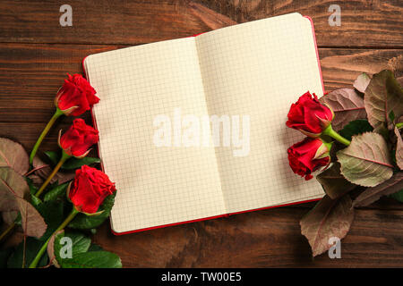 Wunderschöne rote Rosen mit Notebook auf hölzernen Hintergrund Stockfoto